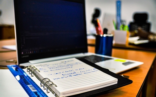 Bild von einem Computer und einem Papier-Notizbuch, das darauf liegt